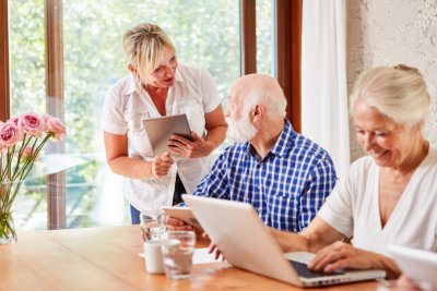 an adult woman talking with the senior man while a senior woman smiling working with her laptop